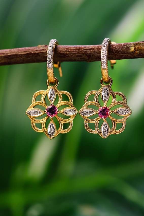 Gold openwork blossom earrings with pink center stones, hanging from a branch