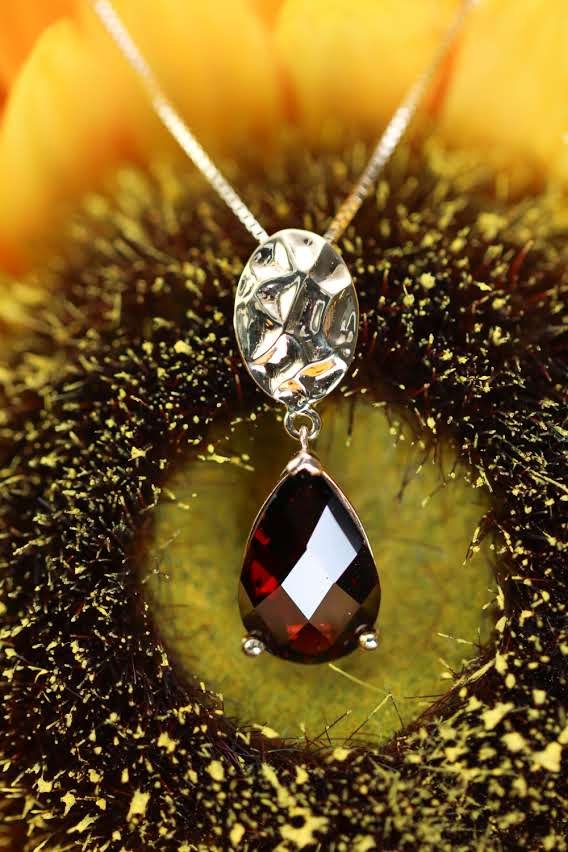 Teardrop garnet pendant resting in the heart of a sunflower