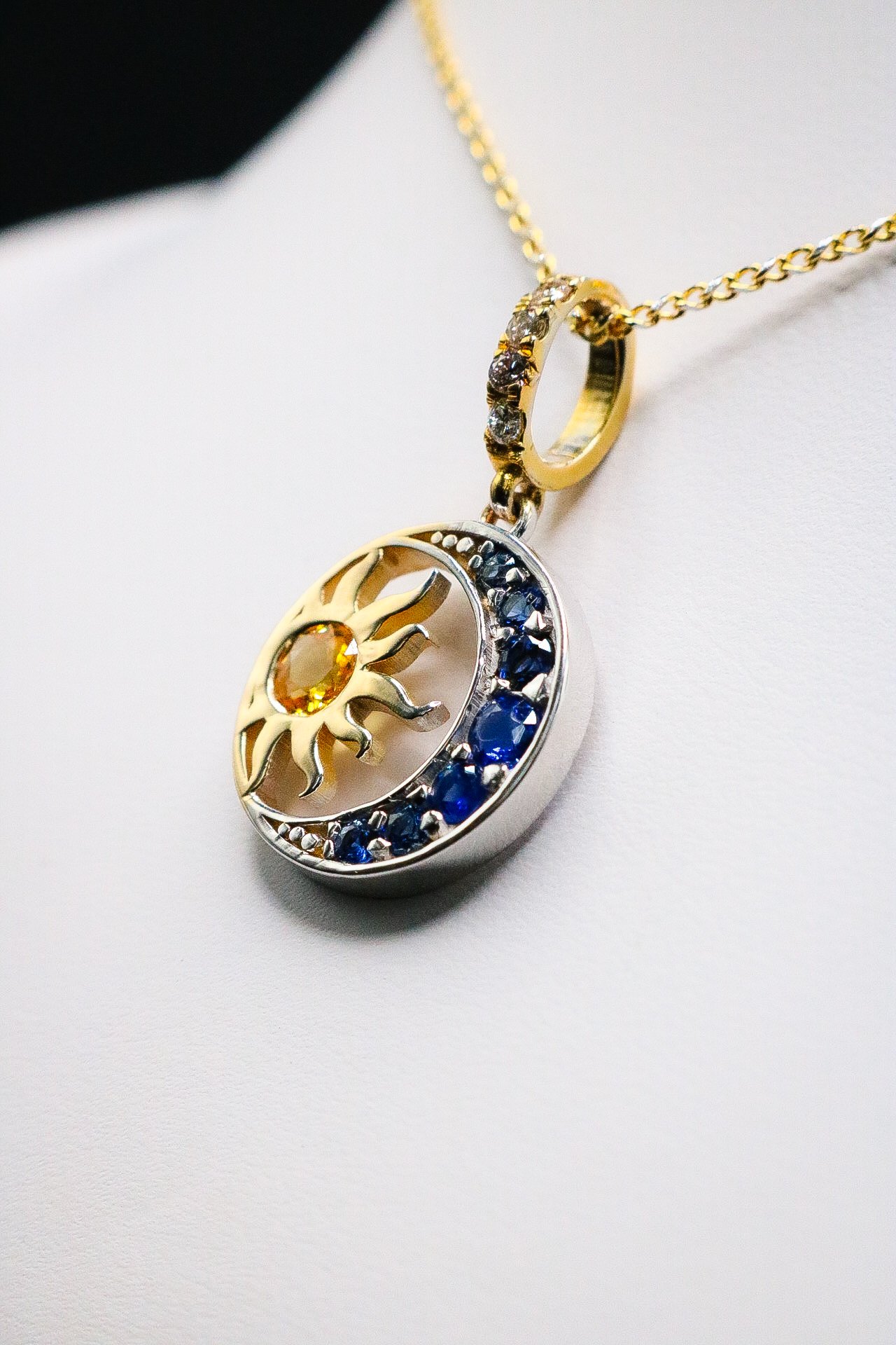 Gold pendant of a sun and crescent moon set with yellow and blue sapphires, hanging from a fine gold chain