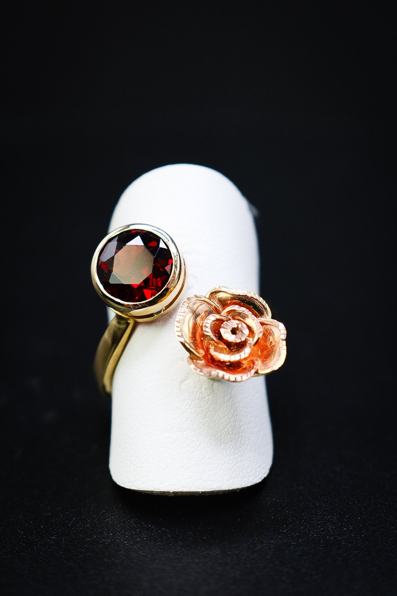 Gold ring with a round garnet beside a sculpted rose in rose gold