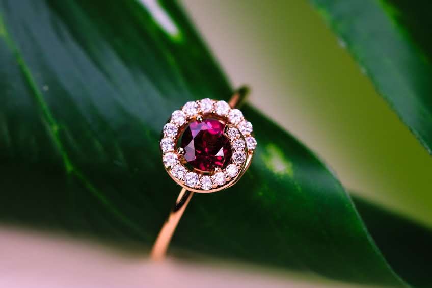 Rose gold ring with a tourmaline and natural diamond halo resting on a green leaf